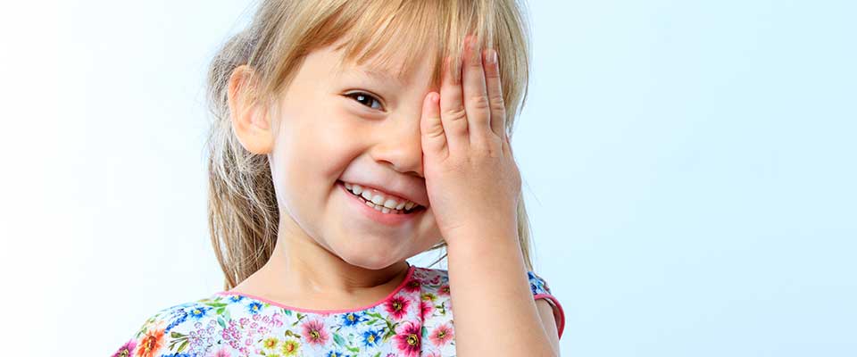 Elementary school girl smiles as she playfully covers one eye.