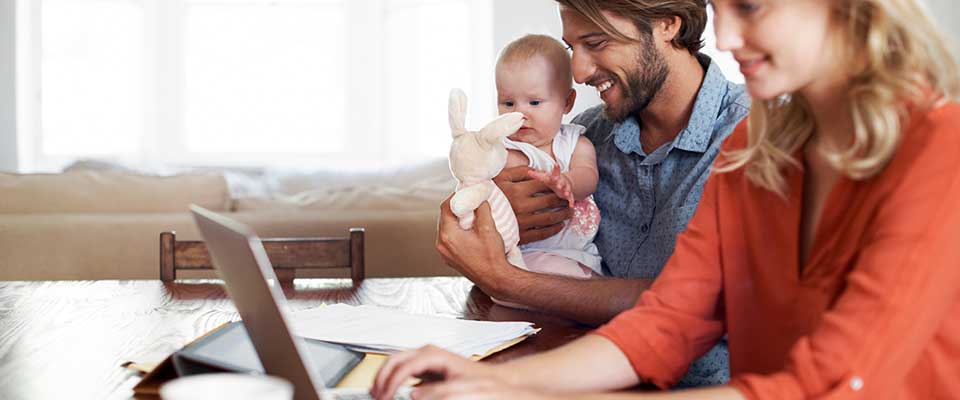 Happy young couple looking at their health savings account on a laptop with their baby girl.