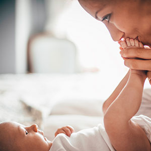 Woman smiles and kisses her baby's feet, reducing signs of postpartum depression.