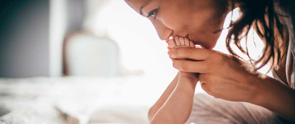 Woman smiles and kisses her baby's feet, reducing signs of postpartum depression.