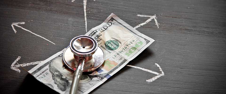 A stethoscope lies atop a hundred dollar bill.