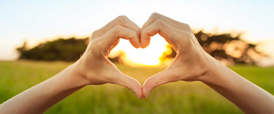 Sunlight filters through a woman's hands in the shape of a heart.