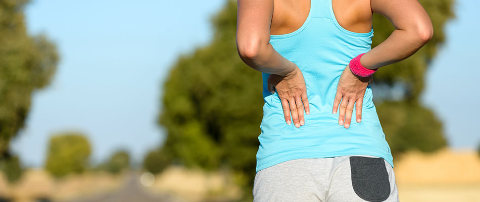 A female runner stops by the side of the road and stretches her lower back.