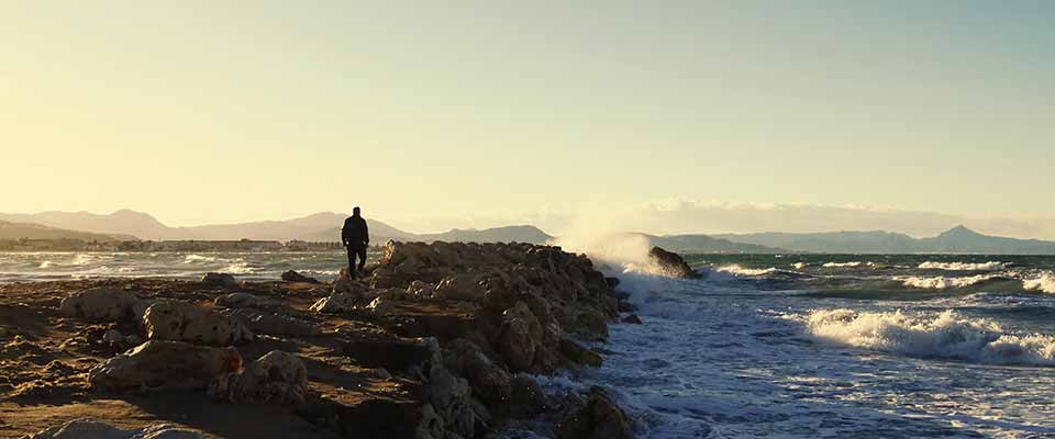 A man walks to the sea on the breakwater during sunset, to relieve his physical symptoms of stress.