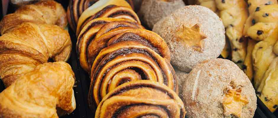 Several rows of pastries, including croissants and cinnamon rolls, line a tabletop.