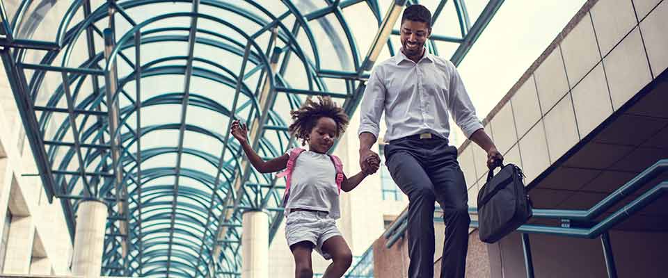 A father runs with his daughter down a flight of stairs, with the sun shining through the glass ceiling behind them, in his attempt to get more steps per day.