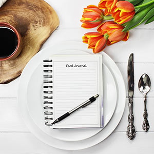 A pen and journal sit on a fancy white table between a set of silverware and a cup of coffee.