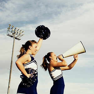 Two young cheerleaders at a high school game show their support with pom poms and a microphone.