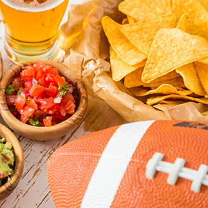 Chips, salsa, beer, and a football sit on a wooden table.