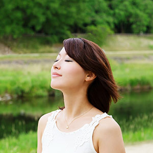 A girl with black hair practices deep breathing in the middle of a field.