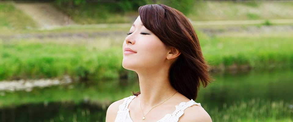 A girl with black hair practices deep breathing in the middle of a field.