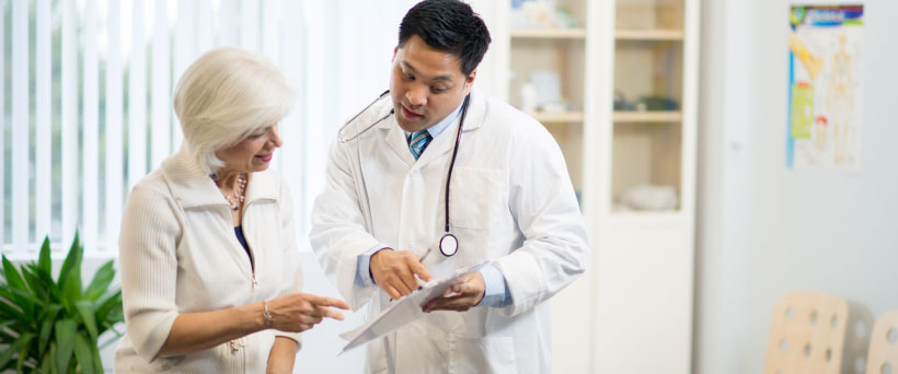 A male doctor showing a paper report to a elderly woman in an office setting.