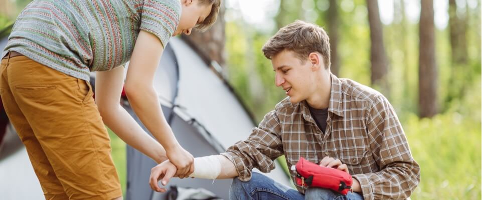 Boy wrapping a bandage on another boy's arm.